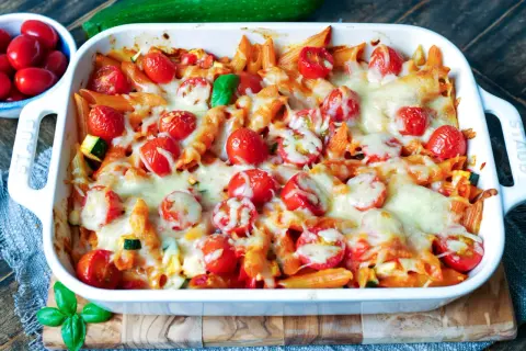 Ein köstlicher nudelauflauf vegetarisch mit Penne, Kirschtomaten und geschmolzenem Käse in einer weißen Auflaufform.
