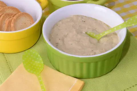 Un cremoso puré de berenjena servido en un cuenco verde, acompañado de galletas tostadas en un cuenco amarillo.