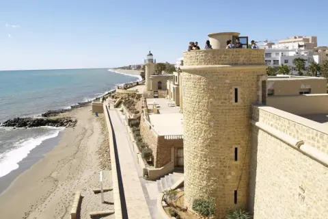 Torreón y faro en el **puerto de Roquetas de Mar**, con playa y mar Mediterráneo al fondo.