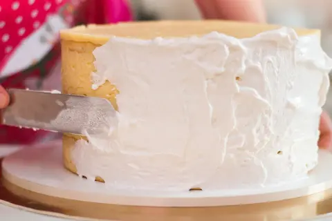 Nakładanie puszystego tynku Milky Way na tort. Kremowa masa pokrywa boki ciasta, tworząc apetyczny wygląd.