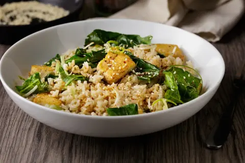 Deliciosa ensalada de arroz con trozos de tofu dorado, espinacas frescas y semillas de sésamo. Un plato nutritivo y lleno de sabor.