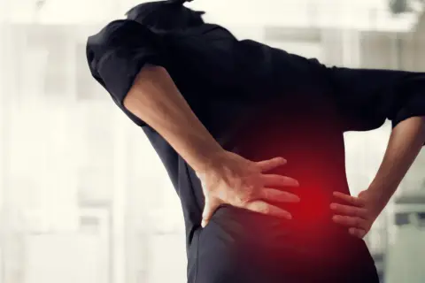 Osoba w czarnej bluzce odczuwa silne drętwienie pleców, trzymając się za bolący odcinek lędźwiowy.