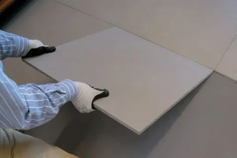 Mains gantées plaçant une nouvelle dalle pour la coller sur du carrelage existant.