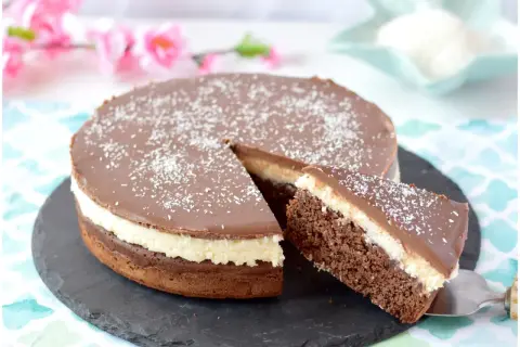 Deliziosa torta cocco e cioccolato con glassa lucida e cocco grattugiato. Una fetta è già servita.