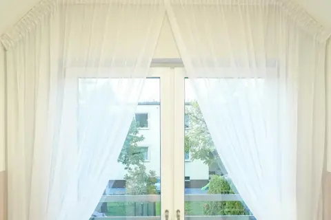 Delikatne, białe firanki upięte na karniszu nad oknem w kuchni, tworzące subtelny efekt.