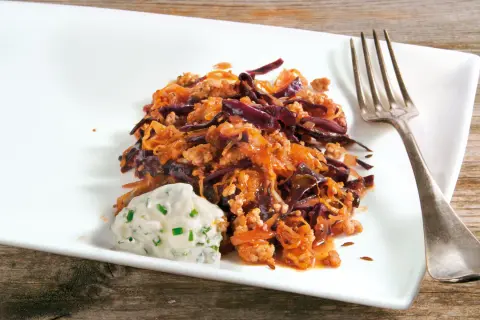 Herzhafte Krautpfanne mit Hackfleisch, serviert mit einem Klecks Kräuterquark und einer Gabel auf einem weißen Teller.