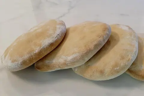 Quatre pains arabes dorés, légèrement saupoudrés de farine, prêts à être garnir.
