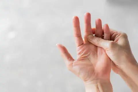 Hand massiert einen schmerzenden Finger, der auf eine Prellung hindeutet.