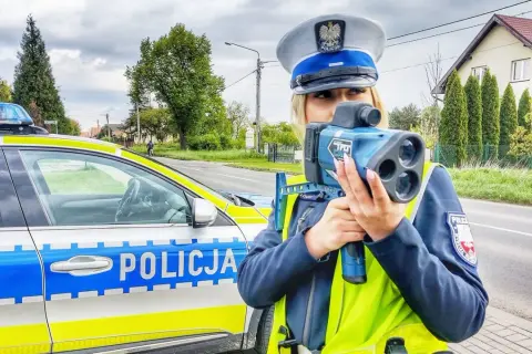 Policjantka z radiowozem i taryfikatorem mierzy prędkość na drodze.