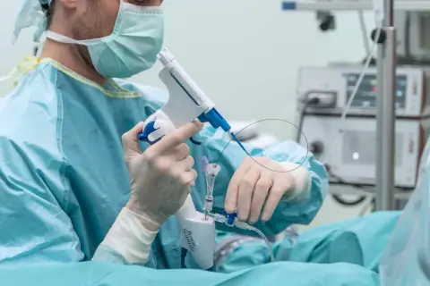 Chirurg w masce i rękawiczkach przygotowuje się do biopsji prostaty, trzymając specjalistyczny przyrząd.