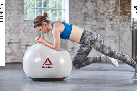 Kobieta w sportowym stroju wykonuje ćwiczenie w podporze na piłce Reebok.