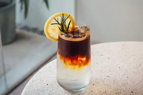 Orzeźwiające espresso z tonikiem, podane z plasterkiem cytryny i gałązką rozmarynu, z lodem w szklance.