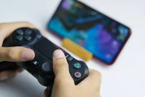 Ręce trzymające kontroler DualSense, gotowe do gry na telefonie. Dowiedz się, jak podłączyć pada PS5 do telefonu, by cieszyć się grami mobilnymi na nowym poziomie.