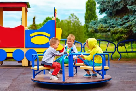 Trzech chłopców bawi się na karuzeli na kolorowym placu zabaw.