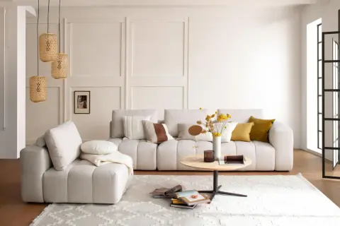 Gemütliches Wohnzimmer mit beiger Couch, Korb-Lampen und einem runden Tisch. Perfekt für slow living einrichtung.