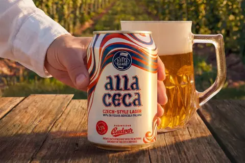 Mano che tiene una lattina di Budweiser ceca "Alla Ceca", con una birra in un boccale sullo sfondo.