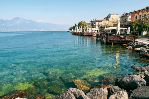 Lungolago di Gardone Riviera: cosa vedere? Case colorate, ristoranti con tavoli all'aperto e il lago cristallino.