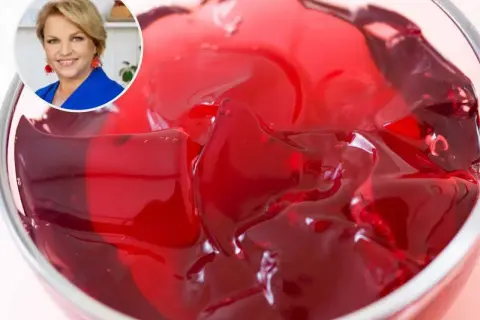 Czerwona galaretka w pucharku, obok uśmiechnięta kobieta. Dowiedz się, ile czasu tężeje galaretka w zamrażarce.