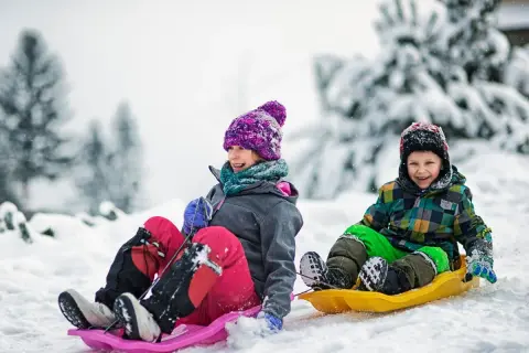 Dzieci z uśmiechem zjeżdżają na sankach po ośnieżonym stoku. Idealne miejsce, gdzie na ferie z dziećmi!