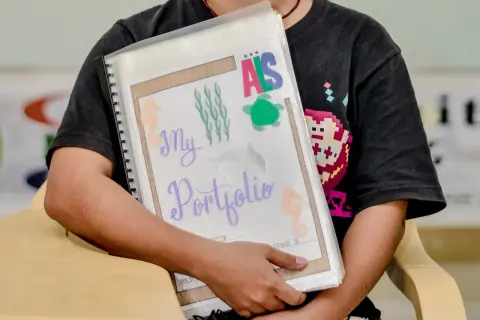 Ein Kind hält ein bunt gestaltetes Portfolio für den Kindergarten mit Seepferdchen und Schildkröten.
