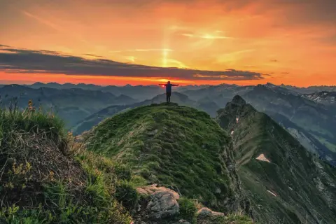 Sonnenuntergang auf der Kanisfluh Wanderung. Ein Wanderer steht mit ausgebreiteten Armen auf dem Gipfel und genießt den atemberaubenden Ausblick.