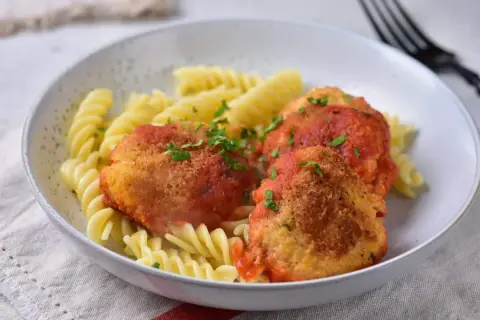 Kotlety w sosie pomidorowym z makaronem fusilli, posypane natką pietruszki.