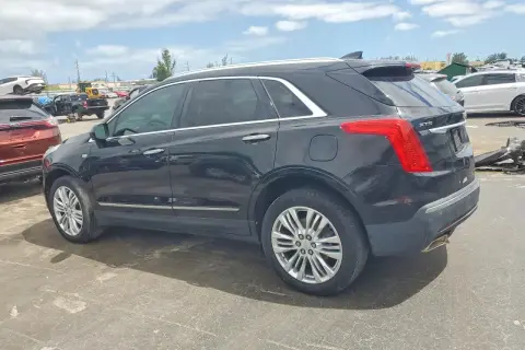 Czarny Cadillac XT5 stoi na placu wśród innych pojazdów.