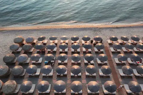 Rzędy leżaków pod słomianymi parasolami na plaży w Sithonii, z morzem w tle.