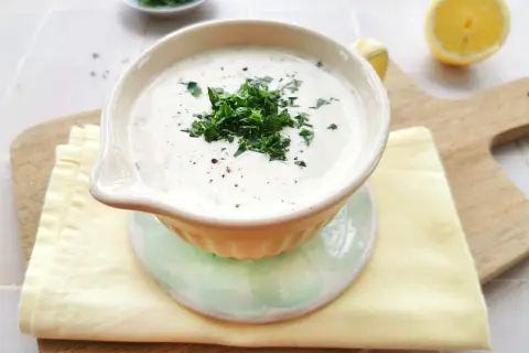 Cremige Schüssel mit frischem Ranch Dressing, garniert mit Petersilie und Pfeffer. Daneben liegen Zitronenspalten und ein Stapel Servietten.