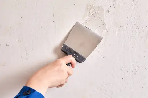 Mano con espátula realizando el alisado de paredes, preparando la superficie para un acabado perfecto.
