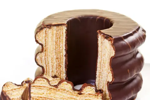 Ein angeschnittener Baumkuchen mit Schokoladenglasur, dessen Schichten die aufwendige Baumkuchen Herstellung zeigen.