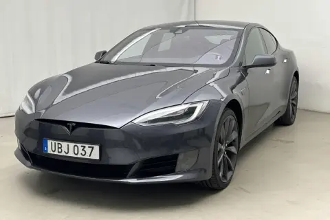 En mörkgrå Tesla Model S, en begagnad elbil med svensk registreringsskylt UBJ 037, står parkerad inomhus.