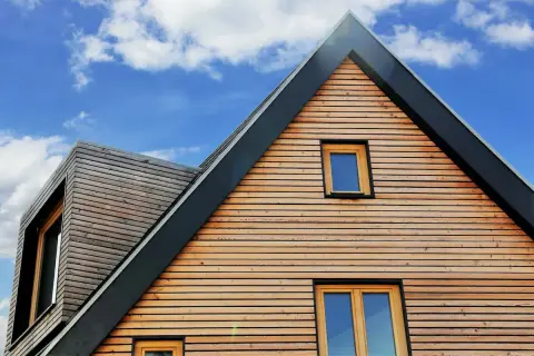 Moderne holzfassade mit horizontalen Holzlamellen und Fenstern unter blauem Himmel mit Wolken.