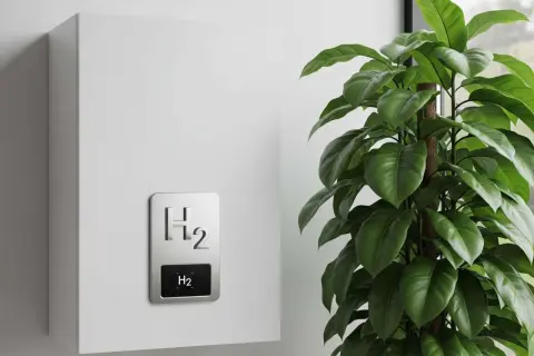 Caldaia ad idrogeno moderna, bianca, con simbolo H₂ in rilievo e display. Accanto, una pianta verde rigogliosa.