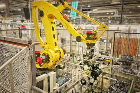 Żółty robot przemysłowy FANUC M-410iC pracuje nad montażem silnika, uosabiając filozofię kaizen toyota w nowoczesnej fabryce.