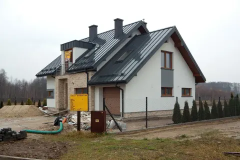 Nowy dom w budowie, widoczny przyłącze napowietrzne, plac budowy z piaskiem i materiałami.