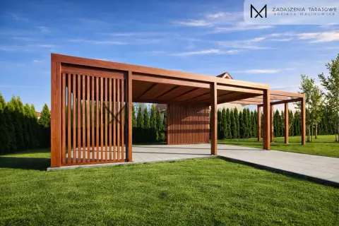 Drewniana pergola z pionowymi żaluzjami na tle zielonego trawnika i niebieskiego nieba.