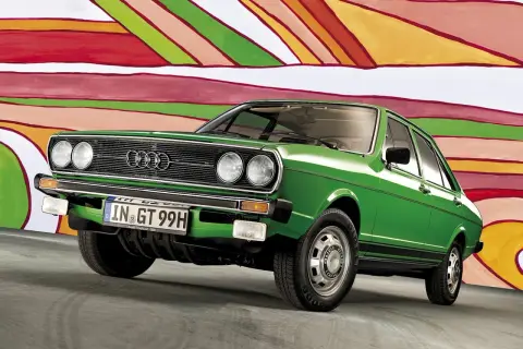 Grön Audi 50 står framför en färgglad, abstrakt bakgrund. Bilen har en klassisk design med kromdetaljer och en svart rand längs sidan.