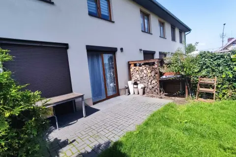 Taras przy domu w Rudzie Śląskiej, z drewnianą ławką, stertą drewna i zielonym ogrodem.