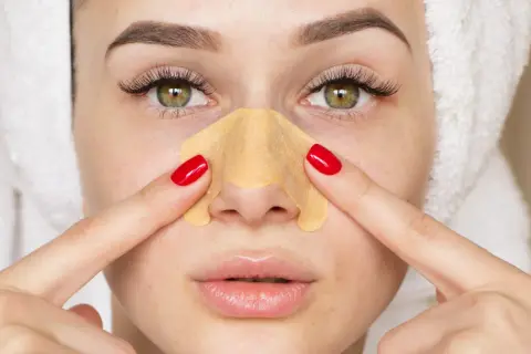 Kobieta z ręcznikiem na głowie stosuje plaster na nos, by pozbyć się głębokich wągrów.