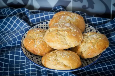 Petits pains à burger dorés et moelleux, saupoudrés de graines de sésame, dans une assiette décorée.