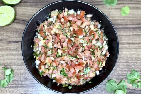 Świeże, kolorowe pico de gallo w czarnej misce, z limonkami i kolendrą na drewnianym tle. Idealne do nachos!