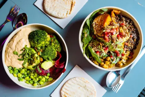 Gesundes Essen nach dem Joggen: Zwei bunte Bowls mit Hummus, Brokkoli, Edamame, Rote Bete, Süßkartoffel, Linsen und Granatapfelkernen.