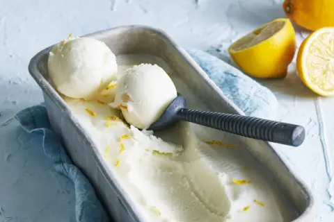 En metallform fylld med krämig italiensk citronsorbet, garnerad med citronskal. Två skopor är upptagna med en skopa.
