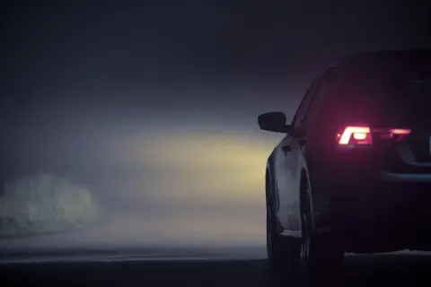 Vue arrière d'une voiture dans le brouillard, feux arrière allumés. L'emplacement des feux de voiture est bien visible.