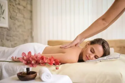 Une femme détendue reçoit un massage du dos, avec des orchidées roses et des huiles de massage à proximité. Offrez-vous un abonnement massage pour un bien-être continu.