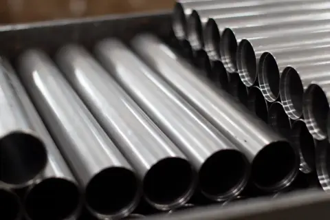 Rury ze stali kwasoodpornej ułożone w pojemniku. Ich gładka, metaliczna powierzchnia odbija światło, tworząc wrażenie czystości i precyzji.