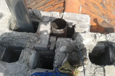 Czyszczenie komina z kwasówki. Widoczna szczotka kominiarska i fragmenty dachu.