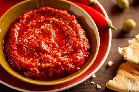 Pikantny sos adżika w miseczce, obok papryczek chili i oliwek. Idealny do pieczywa.