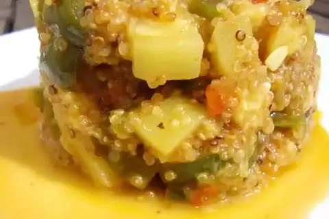 Un délicieux risotto de quinoa aux légumes verts et tomates, servi dans une sauce dorée.